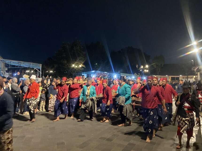 Nighttime street parade with performers in red and blue traditional outfits carrying drums and fans.