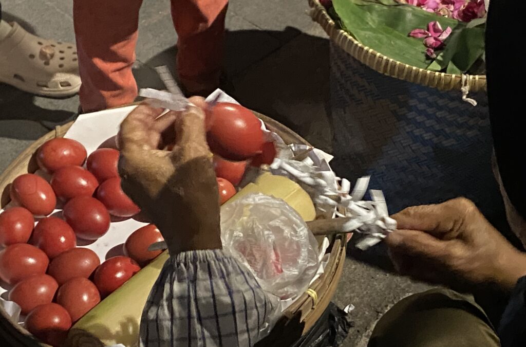 Basket of red tomatoes wrapped in paper, with a hand nearby and a shoe visible in the background.