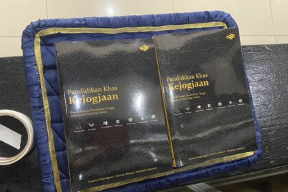 Two black hardcover books with gold Indonesian titles resting on a blue padded mat with a gold trim and patterned covers.