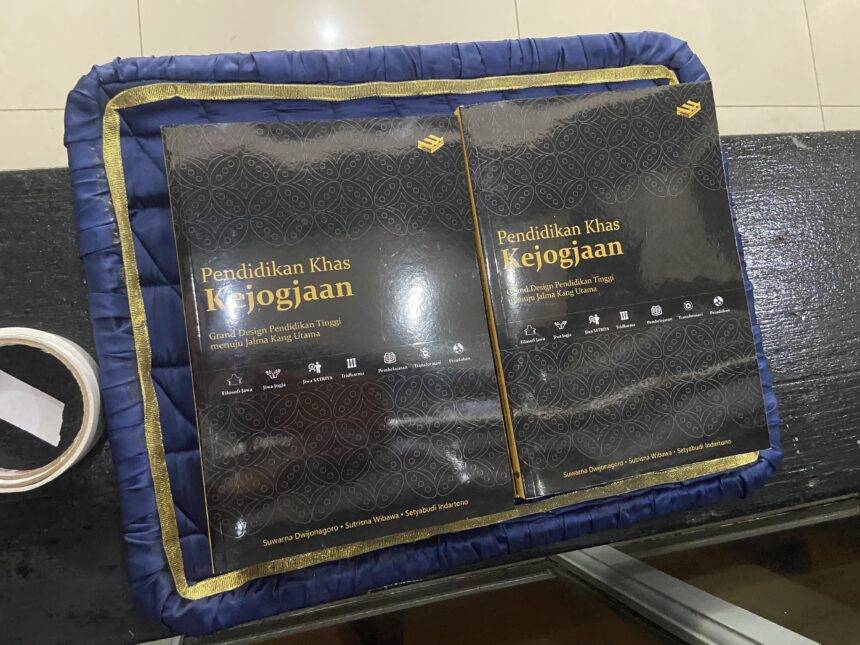 Two black hardcover books with gold Indonesian titles resting on a blue padded mat with a gold trim and patterned covers.