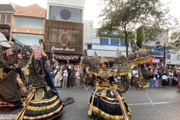 Dancers in elaborate black, gold, and purple costumes perform a street parade as a crowd watches along a city avenue with storefronts in the background.