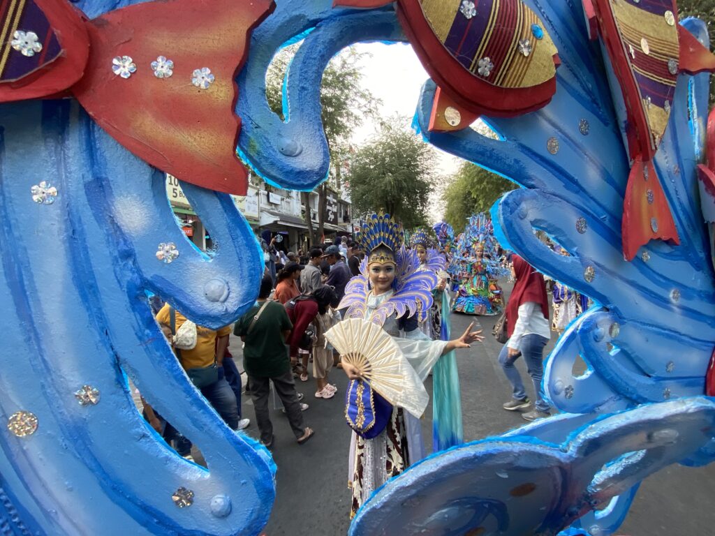 Colorful parade with a blue dragon sculpture framing dancers in lavish purple and gold costumes.