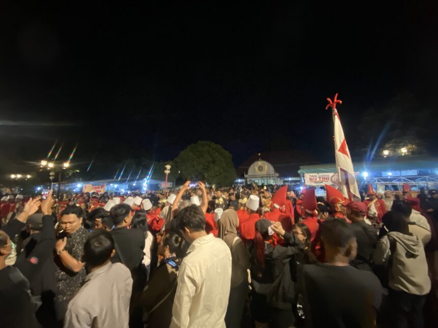 Crowd of people at a night celebration, many wearing red and white, waving flags under bright lights.