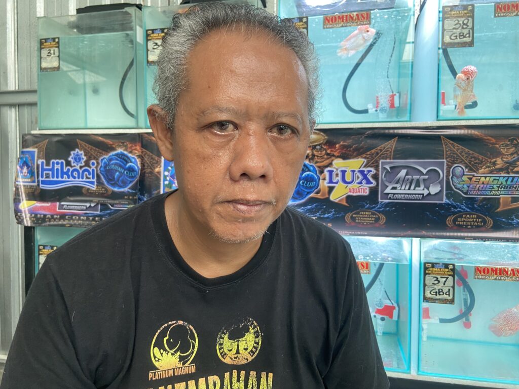 Close-up portrait of a middle-aged man in front of turquoise fish tanks at a shop.