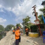 Construction workers in orange uniforms standing along a rocky drainage canal, reviewing plans.
