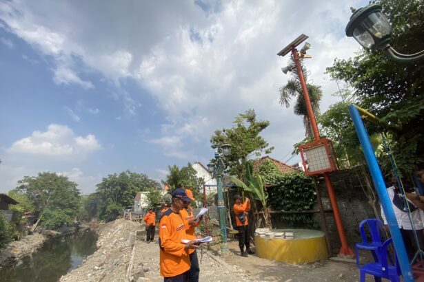 Construction workers in orange uniforms standing along a rocky drainage canal, reviewing plans.