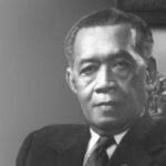 Black-and-white formal portrait of a man in a dark suit seated in an ornate chair.