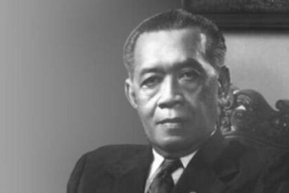 Black-and-white formal portrait of a man in a dark suit seated in an ornate chair.