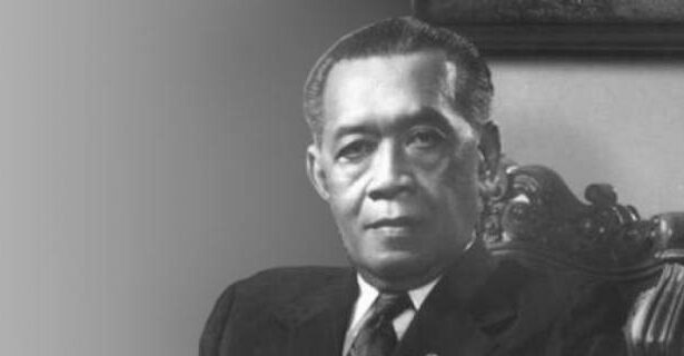 Black-and-white formal portrait of a man in a dark suit seated in an ornate chair.