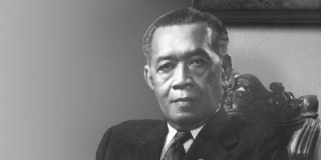 Black-and-white formal portrait of a man in a dark suit seated in an ornate chair.