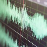 Close-up of a teal audio waveform on a dark grid background with a red cursor line.