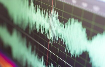 Close-up of a teal audio waveform on a dark grid background with a red cursor line.