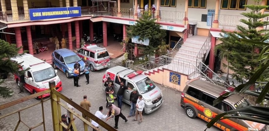 School courtyard with multiple ambulances and staff gathered near the building entrance.