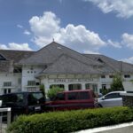 Front view of Rumah Sakit Bethesda hospital with white facade and tiled roof under a blue sky.