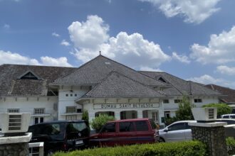 Front view of Rumah Sakit Bethesda hospital with white facade and tiled roof under a blue sky.