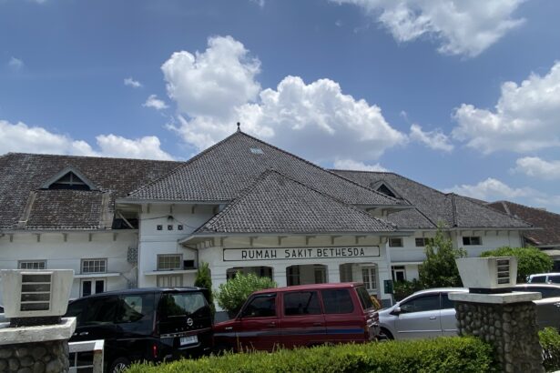 Front view of Rumah Sakit Bethesda hospital with white facade and tiled roof under a blue sky.