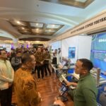 Crowded exhibition hall with people browsing booths and a large blue tech banner on the right side.