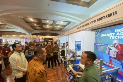 Crowded exhibition hall with people browsing booths and a large blue tech banner on the right side.