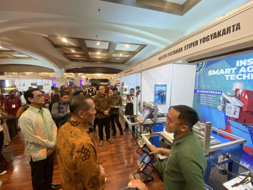 Crowded exhibition hall with people browsing booths and a large blue tech banner on the right side.