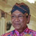 Indonesian man wearing a bright batik shirt and traditional head wrap, smiling indoors at an event.