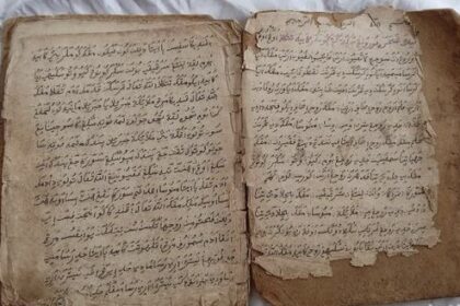 Open old book with handwritten script in Arabic on yellowed, torn pages with frayed edges.