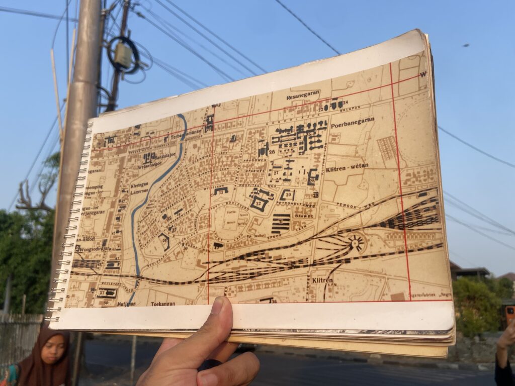 Spiral-bound city map held up by a hand outdoors, showing streets and a river with a clear blue sky behind.