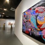 Large, vibrant abstract mural on a gallery wall beside a group of performers in yellow outfits in a white-walled gallery.