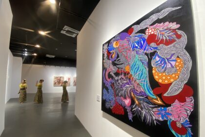 Large, vibrant abstract mural on a gallery wall beside a group of performers in yellow outfits in a white-walled gallery.