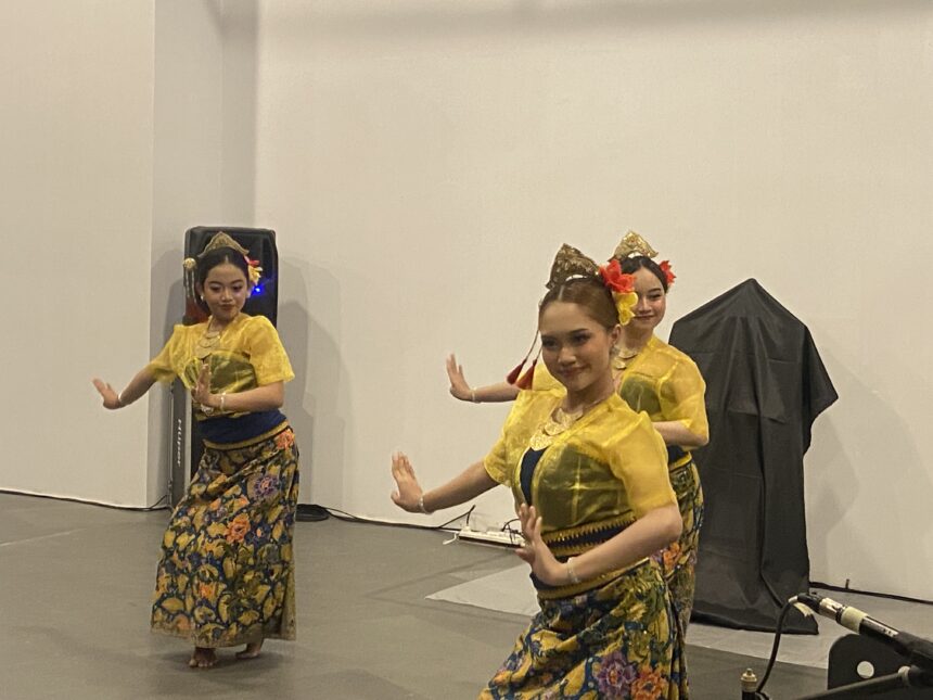 Group of young women in bright yellow traditional costumes dancing on a stage, hands raised in graceful poses with floral headpieces and colorful skirts.