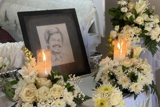 Framed portrait of a smiling person surrounded by white flowers and glowing candles at a funeral arrangements display
