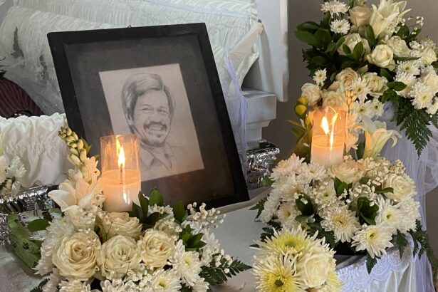 Framed portrait of a smiling person surrounded by white flowers and glowing candles at a funeral arrangements display