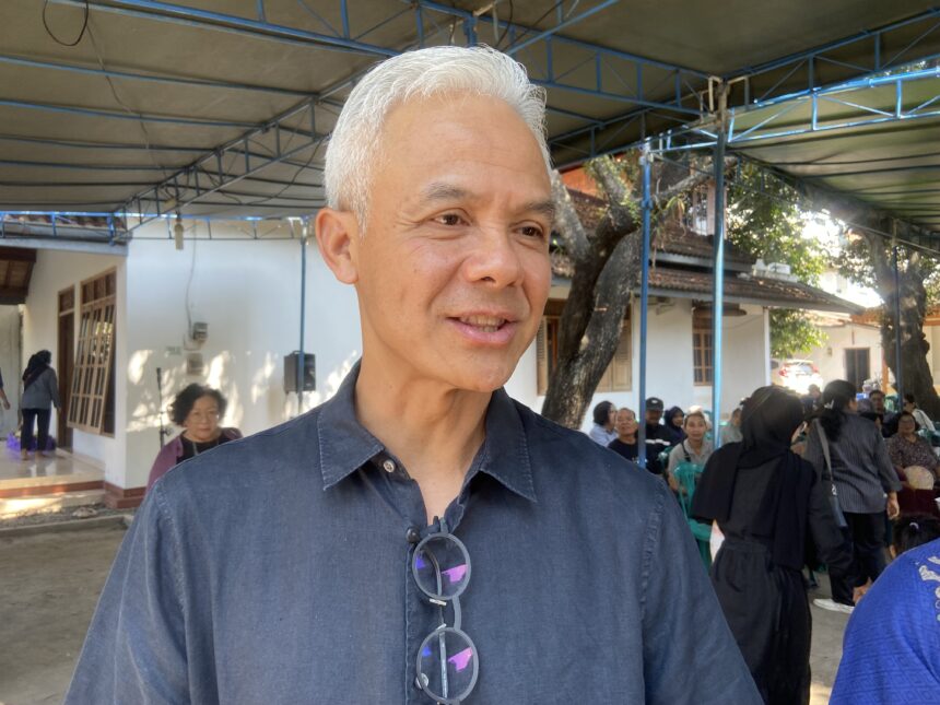 Close-up of a smiling man with white hair and glasses hanging from his shirt, at an outdoor gathering under a blue framework canopy.