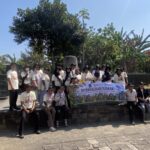 Group of people in matching light-colored shirts posing on stone steps outdoors, holding a large banner for a group event under a sunny sky.