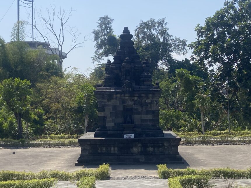 Stone tiered monument in a park, surrounded by trees and a clear blue sky behind it.