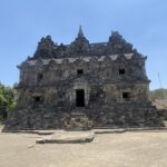 Ancient stone temple with a tiered roof and small rectangular openings, set under a clear blue sky.
