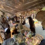 Market stall with women in hijabs selling snacks in clear bags under a plastic-covered roof.
