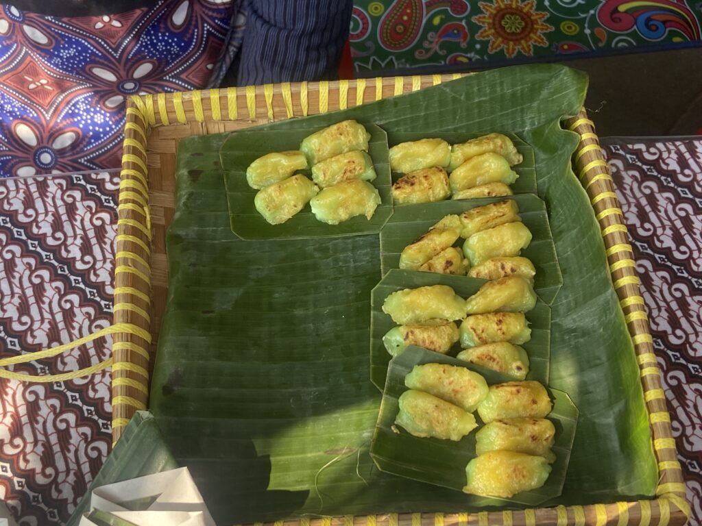 Small yellow-green fried pastries arranged on banana leaves in a woven basket display.