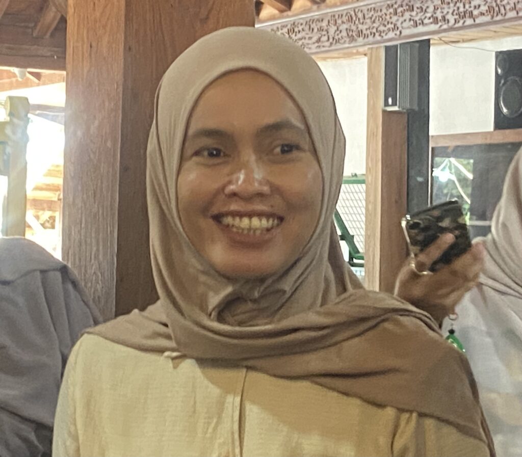 Close-up of a smiling woman wearing a beige hijab indoors.
