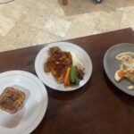 White plate with glazed chicken, mashed potatoes, and carrot and green bean sides on a wooden table.