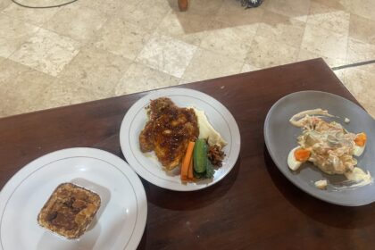 White plate with glazed chicken, mashed potatoes, and carrot and green bean sides on a wooden table.