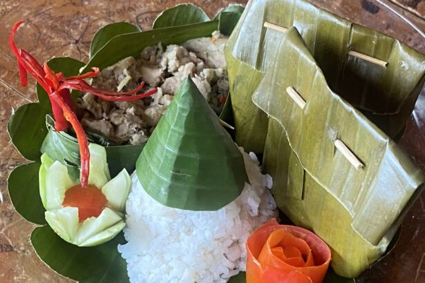 Banana leaf pocket opened to reveal sticky rice with savory filling, garnished with cucumber and carrot rose on a wooden plate.