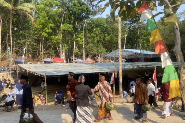 People in traditional clothing carrying woven baskets at an outdoor festival with colorful flags and stalls under trees.