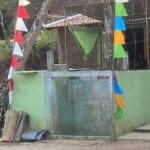 Green wall with a doorway, a brick structure, and colorful triangular fabric flags strung along a line outside.