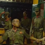 Diorama of soldiers in green uniforms; a man seated with arms extended while others surround him.