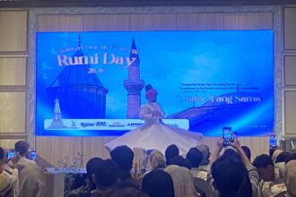 Large blue stage screen displaying 'Rumi Day 2025' with a crowd in front, many people recording with phones.