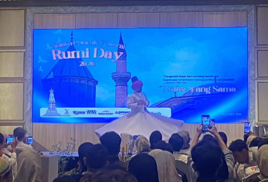 Large blue stage screen displaying 'Rumi Day 2025' with a crowd in front, many people recording with phones.