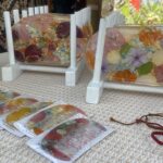 Clear resin coasters embedded with pressed flowers on a light wooden stand and beige woven surface at a market stall.