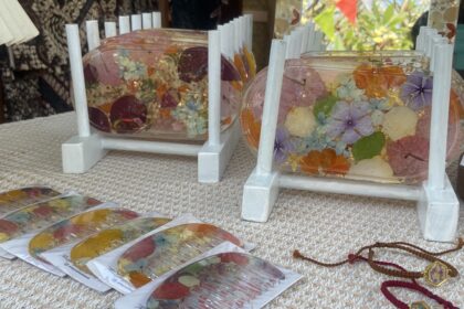 Clear resin coasters embedded with pressed flowers on a light wooden stand and beige woven surface at a market stall.