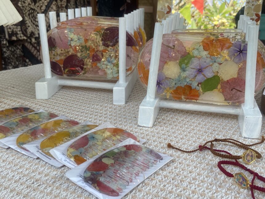 Clear resin coasters embedded with pressed flowers on a light wooden stand and beige woven surface at a market stall.