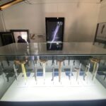 Glass display case holding a row of curved-blade daggers on clear stands in a museum exhibit set-up.